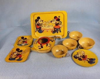 May include: A yellow and black Mickey Mouse themed children's tea set. The set includes a teapot, four cups, four saucers, and a tray. The teapot has a Mickey Mouse head on the lid and the cups and saucers have Mickey Mouse images on them.