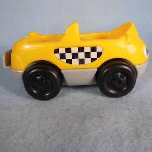 Coche vintage Fisher Price de dos plazas, amarillo, con un cartel a cuadros en el lateral.
