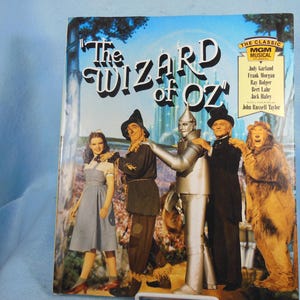 May include: A vintage record album cover featuring the classic MGM musical "The Wizard of Oz". The cover features a colorful illustration of Dorothy, the Scarecrow, the Tin Man, and the Cowardly Lion standing in front of the Emerald City.