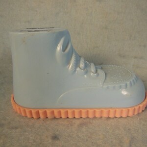 May include: A light blue plastic baby shoe with a pink scalloped edge. The shoe has a lace-up design and a textured sole.