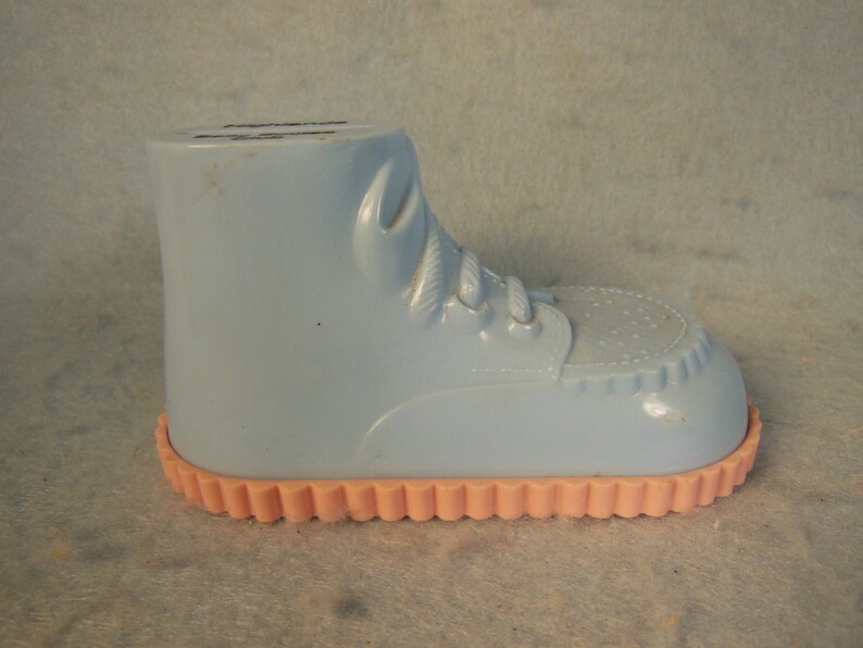 May include: A light blue plastic baby shoe with a pink scalloped edge. The shoe has a lace-up design and a textured sole.