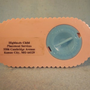 May include: Pink plastic piggy bank with a blue lid that says "OPEN" and "INSERT COIN". The bottom of the bank has the text "Highlands Child Placement Services 5506 Cambridge Avenue Kansas City, MO 64129".