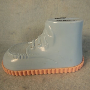 May include: A light blue plastic baby shoe shaped piggy bank with a pink bottom and the text "Highchair" on the side.