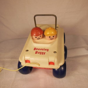 Puede incluir: Un coche de juguete de plástico blanco con ruedas azules y un asa amarilla. El coche tiene dos figuras en los asientos delanteros, una niña con pelo rojo y un niño con pelo amarillo. El coche tiene las palabras "Bouncing Buggy" impresas en la parte delantera.