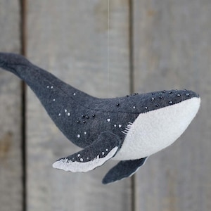 May include: A gray felt whale with white felt on the belly and black beads for eyes. The whale is hanging from a string.
