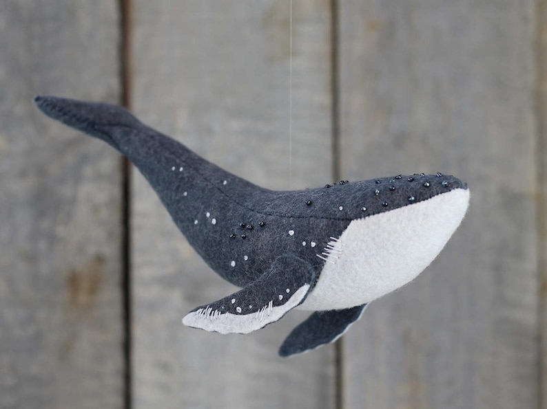 May include: A gray felt whale with white felt on the belly and black beads for eyes. The whale is hanging from a string.