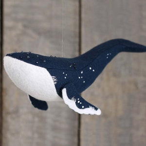 May include: A plush blue whale with white underbelly and black bead accents. The whale is hanging from a string.