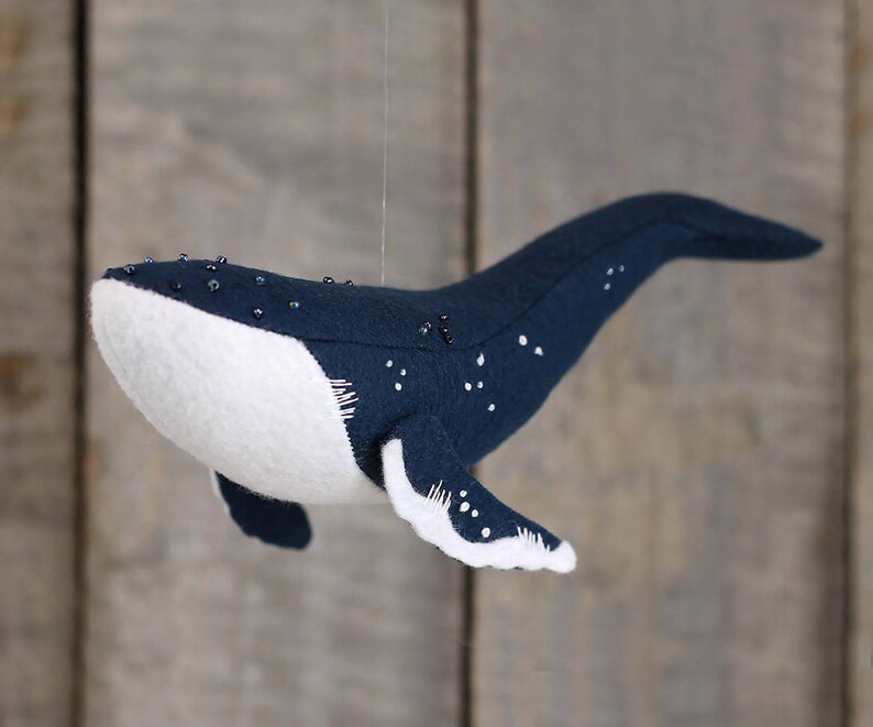May include: A plush blue whale with white underbelly and black bead accents. The whale is hanging from a string.
