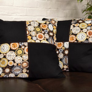 May include: Two black and white cushion covers with a pattern of gold clocks. The cushions are on a brown leather sofa.