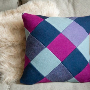 May include: A decorative pillow with a diamond pattern in shades of pink, blue, and purple. The pillow is made of a soft, textured fabric.