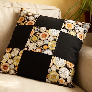 Op de afbeelding: Een zwart en gouden kussen met een geruit patroon met een ontwerp van vintage klokken.