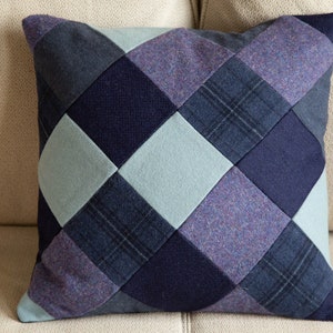 May include: A blue, purple and grey patchwork cushion with a diamond pattern. The cushion is made of different fabrics and has a soft, textured look.