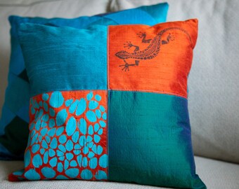 May include: A turquoise and orange patchwork cushion with a lizard design and a pattern of blue circles on an orange background.