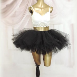 May include: A white lace crop top and a black tulle tutu skirt displayed on a mannequin. The top has delicate lace detailing. The tutu is full and fluffy, creating a layered effect. The mannequin is on a dark wooden stand.