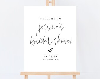 May include: A white sign with black text that reads "Welcome to Jessica's Bridal Shower" with a heart and the date "09.05.21" and the text "Let's celebrate!" The sign is on an easel.