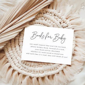 May include: A white card with the text "Books for Baby" in elegant script, surrounded by a woven placemat and dried palm leaves. The card requests guests bring a book instead of a card for the baby.