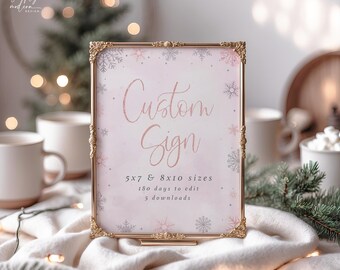 May include: A gold-framed sign with the words "Custom Sign" in a cursive font. The sign has a pink and white watercolor background with snowflake accents. The sign is displayed on a white surface.