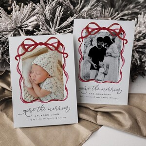 Op de afbeelding: Twee witte kerstkaarten met rode lintframes. Eén kaart toont een slapende baby, de andere een familiefoto. Beide kaarten hebben de tekst "more the merrier" in cursief.