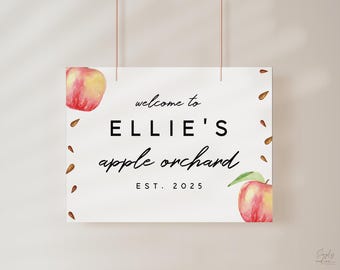 Puede incluir: Un cartel blanco con texto negro que dice "Bienvenido a Ellie's apple orchard est. 2025". El cartel está decorado con manzanas rojas y semillas marrones.