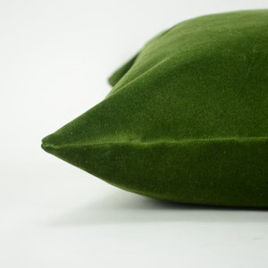 May include: A close-up of a dark green velvet pillow. The pillow is soft and plush, with a smooth, even texture.