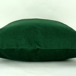 May include: A deep green velvet pillow with a square shape and a smooth, soft texture.