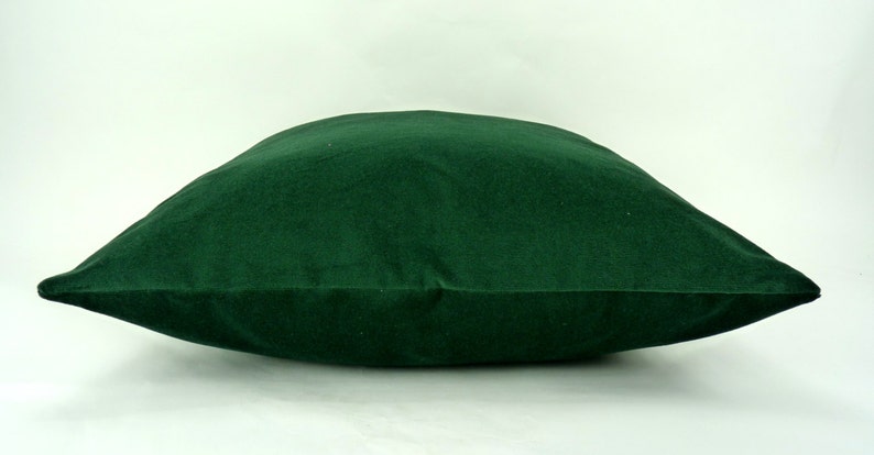 May include: A deep green velvet pillow with a square shape and a smooth, soft texture.