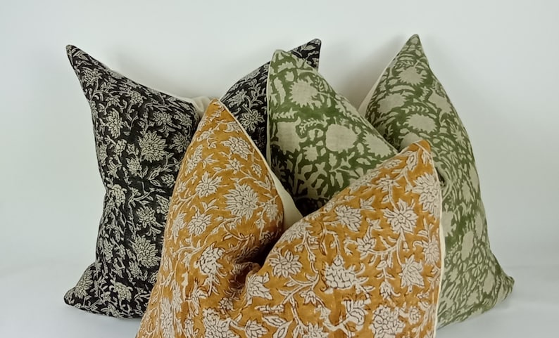 May include: Four decorative throw pillows with floral patterns. The pillows are in shades of black, green, and mustard yellow.