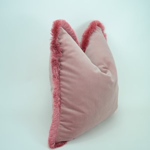 May include: A pink velvet pillow with a fringe trim around the edges.