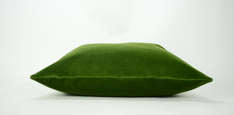 May include: A large, square, green velvet pillow. The pillow is soft and plush, and would be perfect for adding a touch of color and comfort to any room.