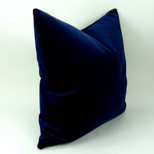 May include: A dark blue velvet pillow with a square shape. The pillow is made of a soft, plush fabric.