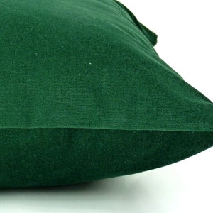 May include: A dark green velvet pillow with a smooth, soft texture. The pillow is folded in half and the seam is visible.