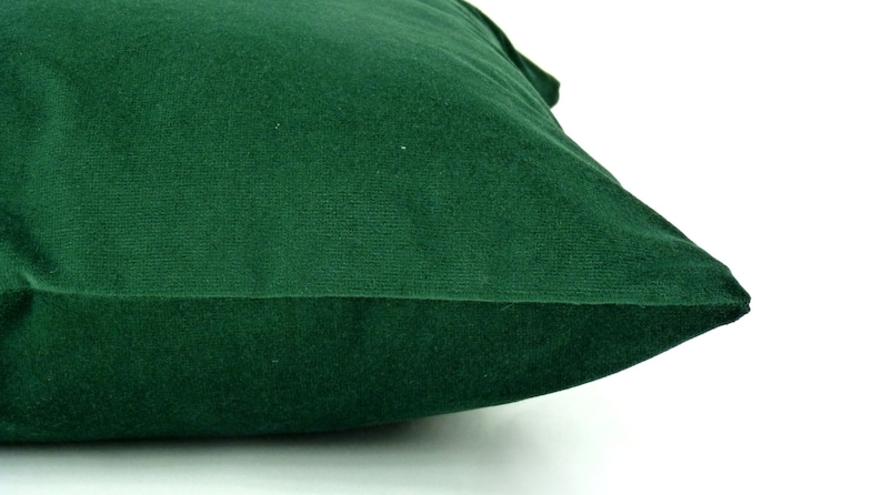 May include: A dark green velvet pillow with a smooth, soft texture. The pillow is folded in half and the seam is visible.