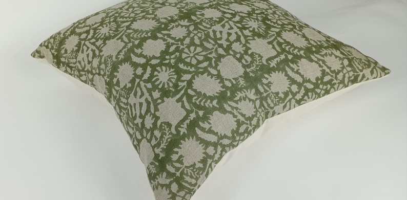 May include: A green and white floral patterned throw pillow with a white border.