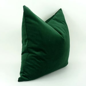 May include: A deep green velvet pillow with a square shape and a slightly pointed top.