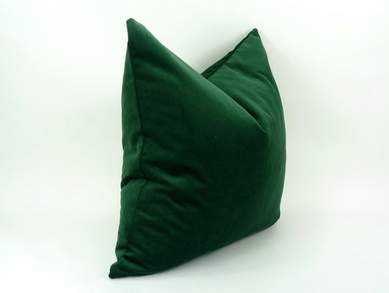 May include: A deep green velvet pillow with a square shape and a slightly pointed top.