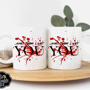 Peut inclure: Deux mugs en c&eacute;ramique blanche avec le texte "...AND THEN I MET YOU" en noir, avec des &eacute;claboussures rouges. Les tasses sont sur un plateau en bois. Le logo Bella Bumble Bee est visible.