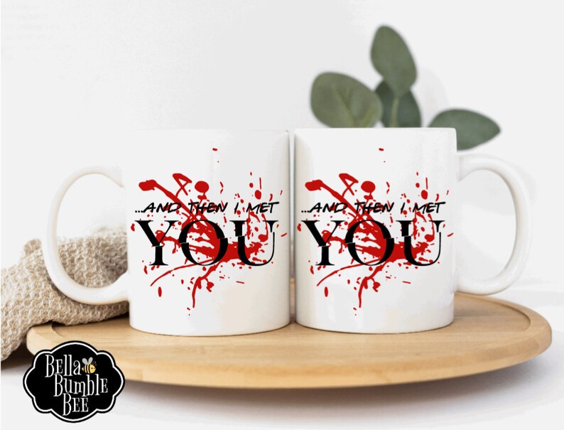 Peut inclure: Deux mugs en c&eacute;ramique blanche avec le texte "...AND THEN I MET YOU" en noir, avec des &eacute;claboussures rouges. Les tasses sont sur un plateau en bois. Le logo Bella Bumble Bee est visible.