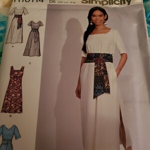 Könnte beinhalten: Ein Schnittmuster für ein Kleid mit einem weißen Kleid und einem bunten Gürtel. Das Schnittmuster ist von Simplicity und ist in Größe 36-44.