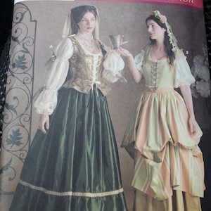 May include: A sewing pattern envelope titled Renaissance Costume Collection featuring two outfits. Outfit A includes a dark green skirt, a gold bodice, and white sleeves. Outfit B features a striped green and peach skirt with a light green bodice.