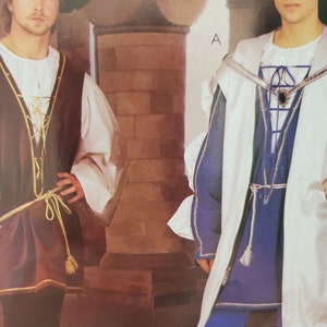 May include: Two medieval costumes are displayed. One features a brown vest with gold trim over a white shirt and brown pants. The other costume is blue and white with a matching blue hat. Both outfits have decorative ties.