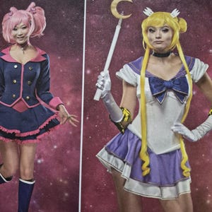 May include: A sewing pattern envelope featuring two costumes. Costume A is a dark blue jacket with pink trim and a matching skirt. Costume B is a white and purple dress with a large blue bow, yellow wig, white gloves, and a crescent moon wand.