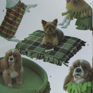 May include: Simplicity pattern 960 featuring no-sew pet clothing and accessories. The image shows dogs wearing various outfits, including a fringed collar, a blanket, and a bed. The pattern includes sizes for all pets.