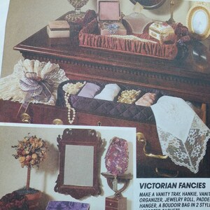 May include: A collection of Victorian-style accessories, including a vanity tray, jewelry roll, and boudoir bag. The image showcases various decorative items, such as a mirror, sachets, and a lace handkerchief, all arranged on a dark wooden surface.
