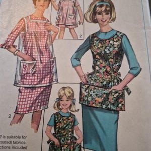 May include: A Simplicity sewing pattern envelope labeled 8809, size Medium 14-16. The illustration displays three variations of a sleeveless apron or pinafore worn over dresses. One apron is clear plastic over a red plaid dress, while others feature floral prints.