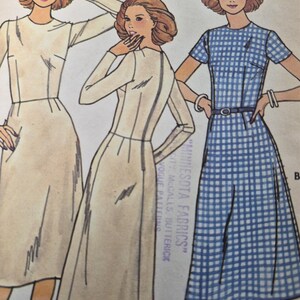 May include: A sewing pattern illustration featuring three dress variations. Two dresses are solid cream with long sleeves and a fitted bodice. The third dress is blue and white gingham with short sleeves, a round neckline, and a thin waist belt.