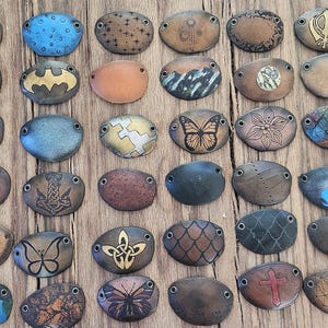 May include: A collection of 48 oval-shaped leather patches with various designs, including butterflies, flowers, geometric patterns, and abstract art. The patches are all brown leather with different coloured designs.