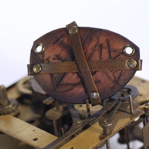 May include: A close-up of a brown leather watch strap with a decorative design. The strap is attached to a metal watch face with gears visible.