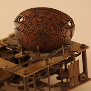 Peut inclure: Gros plan sur un mécanisme d'horloge vintage avec un motif de toile d'araignée en bois sur le dessus. L'horloge est en laiton et possède des engrenages complexes.
