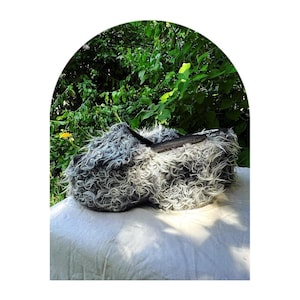 May include: A pair of fluffy gray and black slippers with a zipper detail. The slippers are sitting on a white fabric surface.