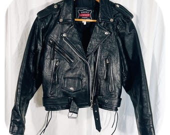 May include: Black leather motorcycle jacket with a zipper closure, multiple pockets, and a belt. The jacket has a label that reads "Biker's Leather Stuff".